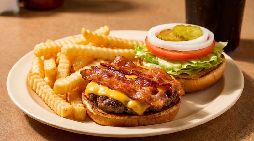 Crinkle-cut fries, a bacon cheeseburger, and an open burger with lettuce, tomato, onion, and pickles.
