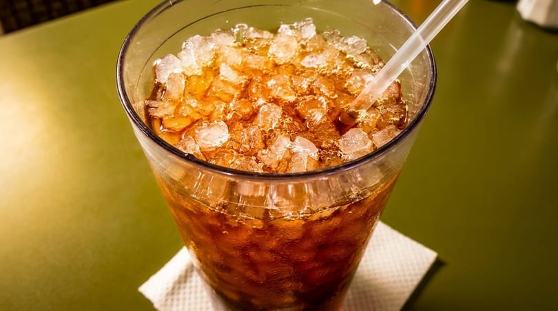 A glass of iced soda with a straw on a green table.