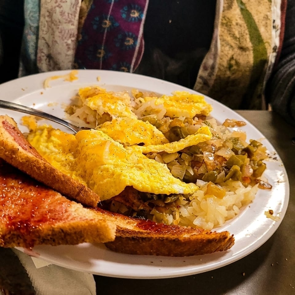 Person eating a breakfast plate of scrambled eggs, hash browns with vegetables, and jam toast.